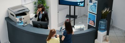 Receptionist working in hospital waiting area and offering support to patients at checkup visit, mother with child having medical appointment with physician. Reception desk at healthcare clinic.